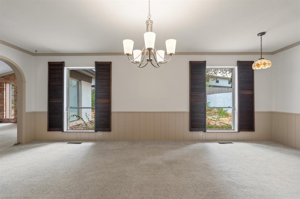 Empty dining room with carpet, paneled walls, shuttered windows, and two hanging lights.