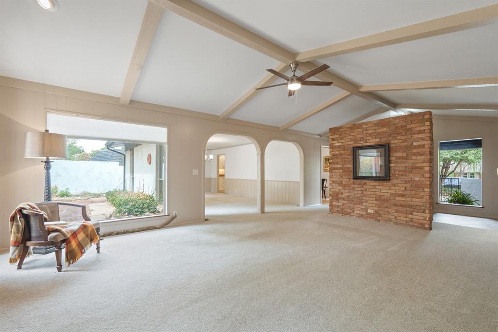 Living room with vaulted beamed ceiling, arched openings, and a brick accent wall.