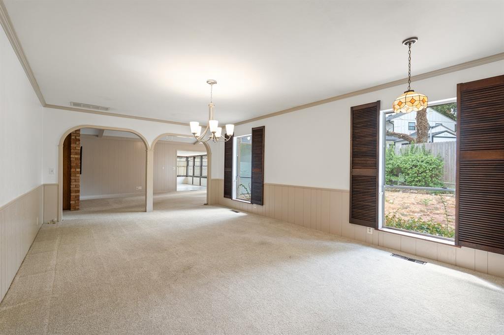 Empty dining room with a chandelier, shuttered windows, and arched openings to adjoining rooms.