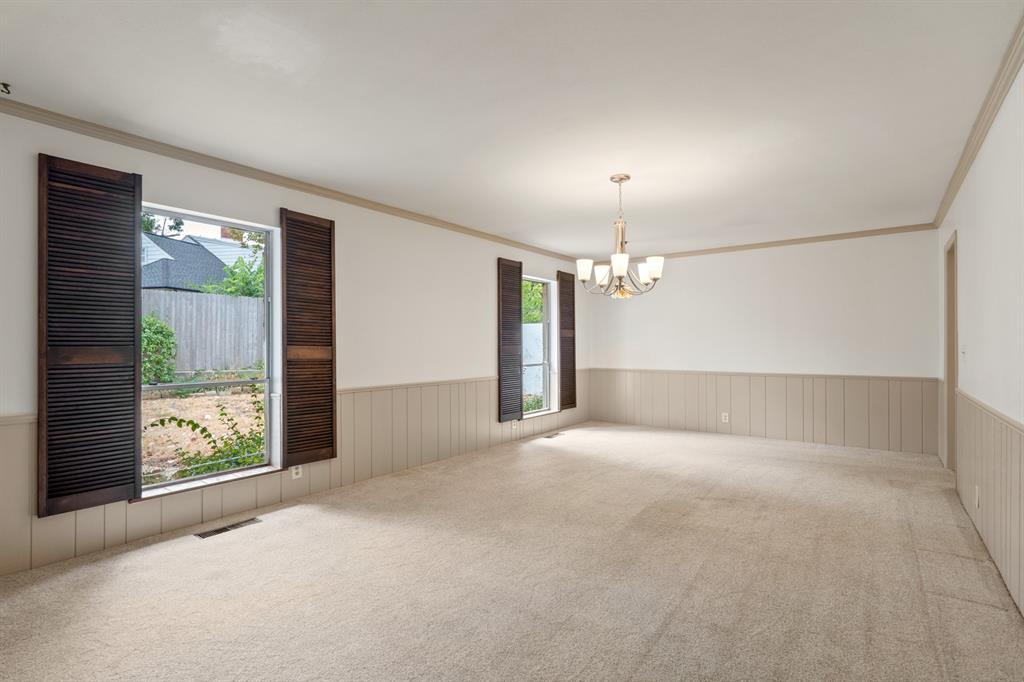 Empty carpeted room with paneled wainscoting, shuttered windows, and a chandelier.