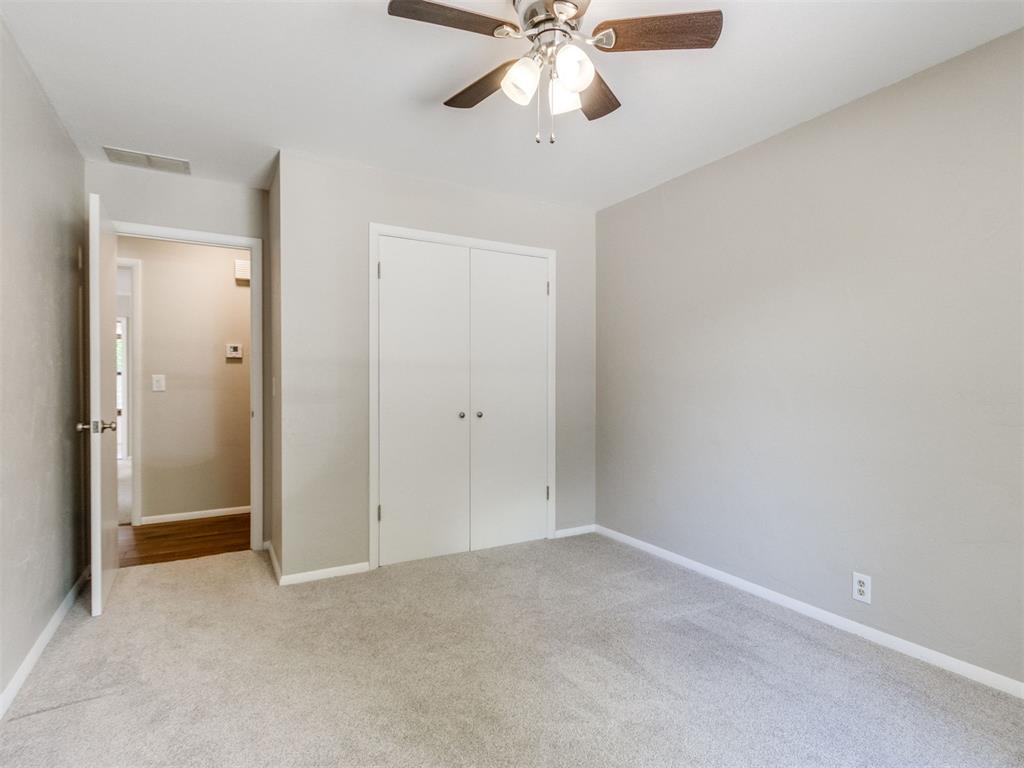 Empty bedroom with beige carpet, double-door closet, and ceiling fan.