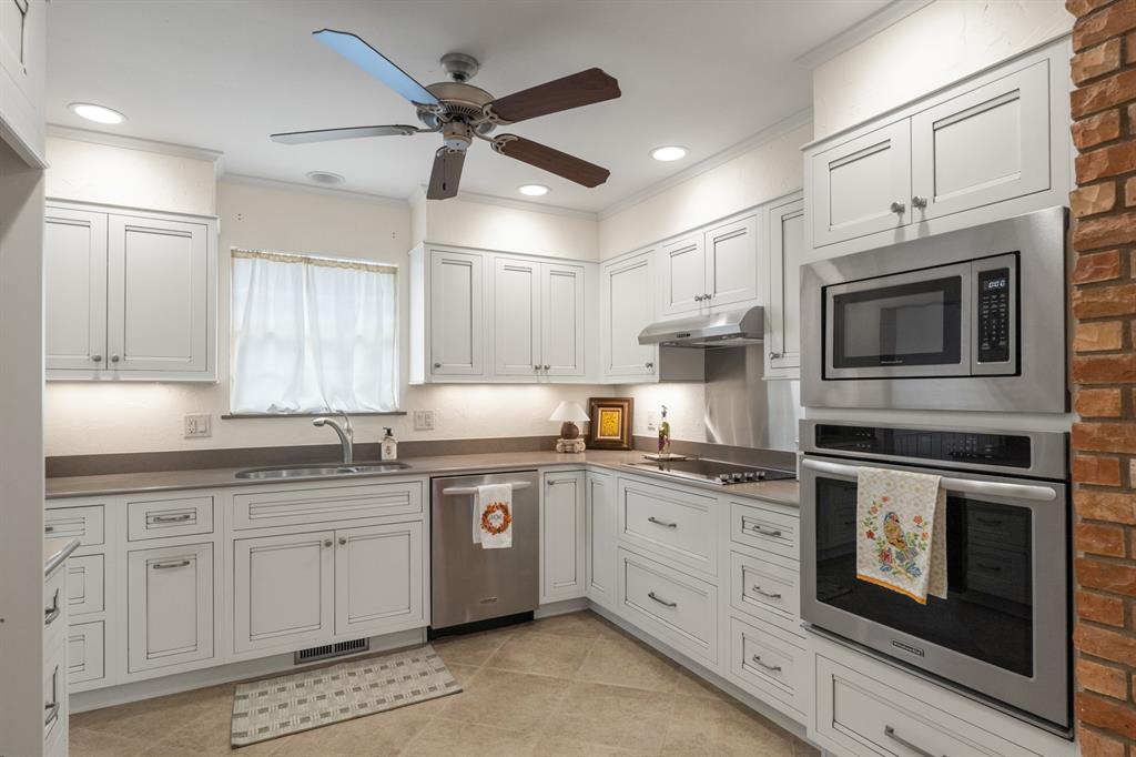 Kitchen with white paneled cabinets, stainless appliances, a curtained window, and a brick accent wall.