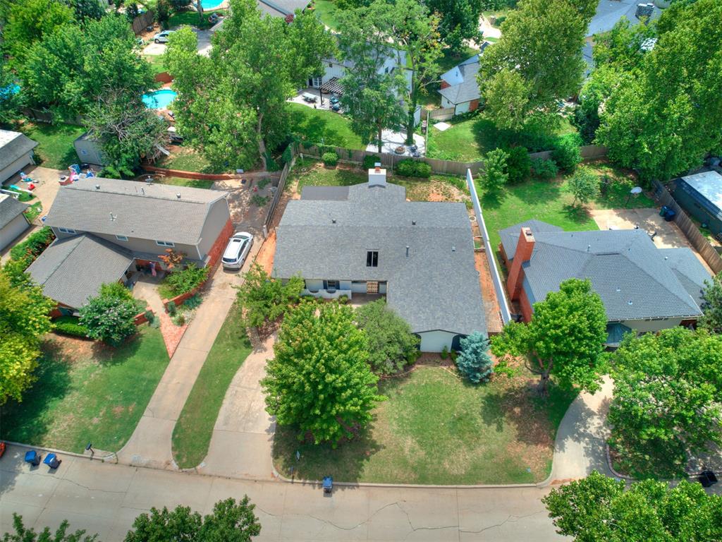 Aerial view of a single-story home with a broad gray roof, mature trees, and a curved street.