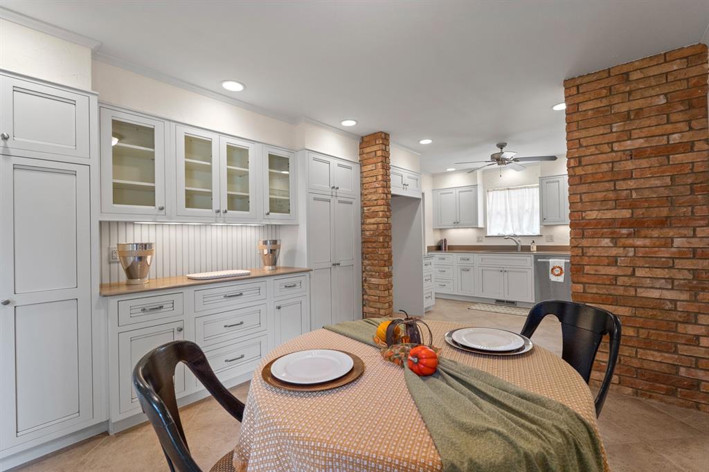 Kitchen with white built-in cabinetry, a curtained sink window, brick columns, and a set dining table.