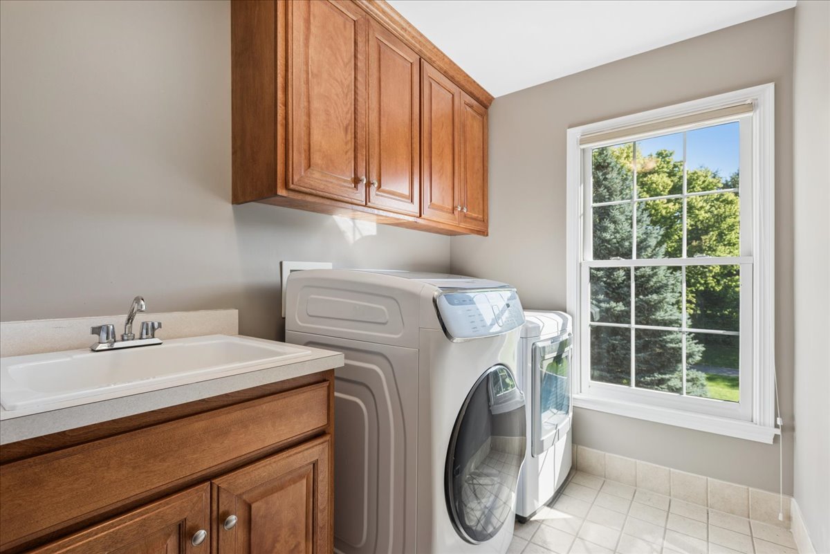 Laundry room with front-loading washer and dryer, wooden cabinets, utility sink, and a large window.
