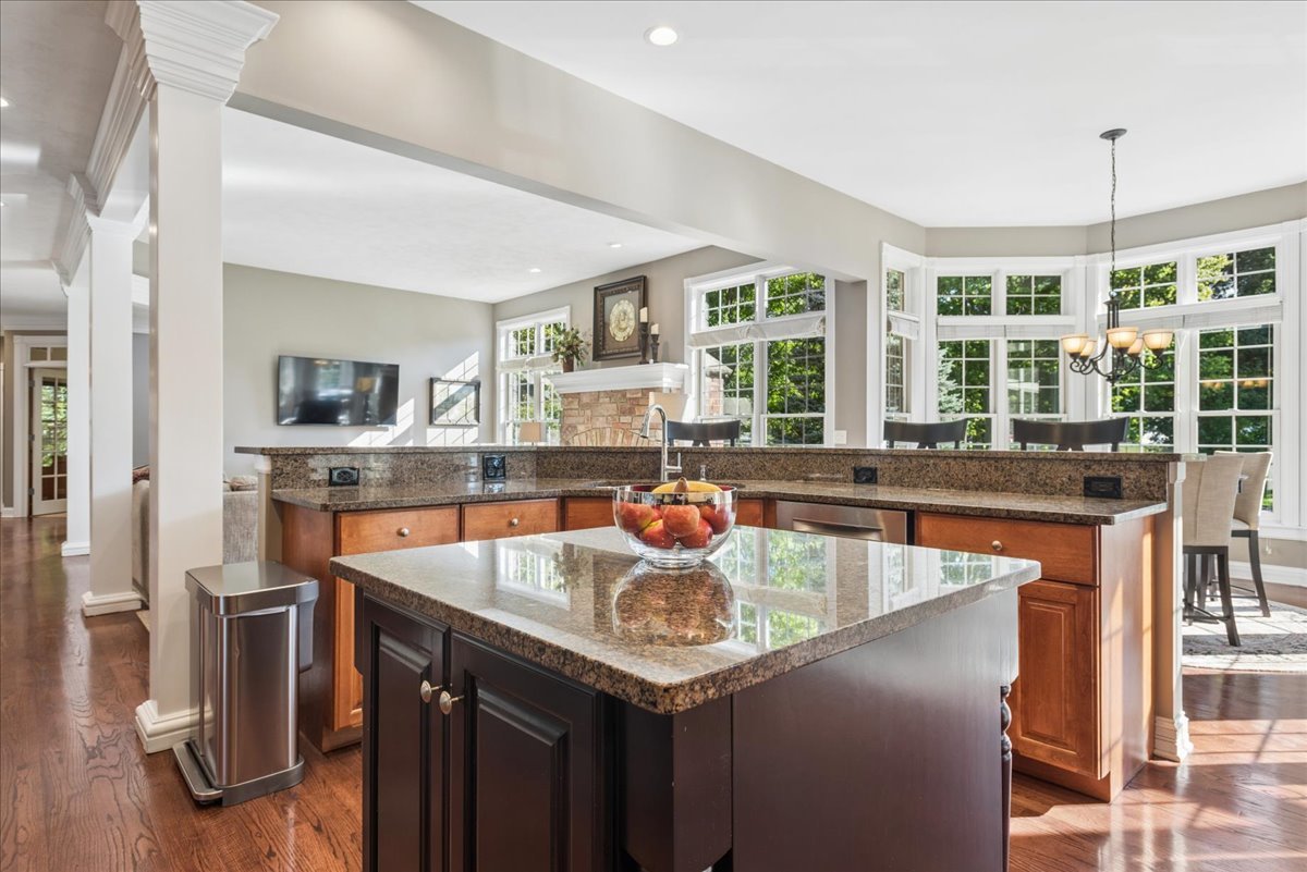 Kitchen with a large granite island, warm wood cabinets, and a sunlit bay-window dining area.