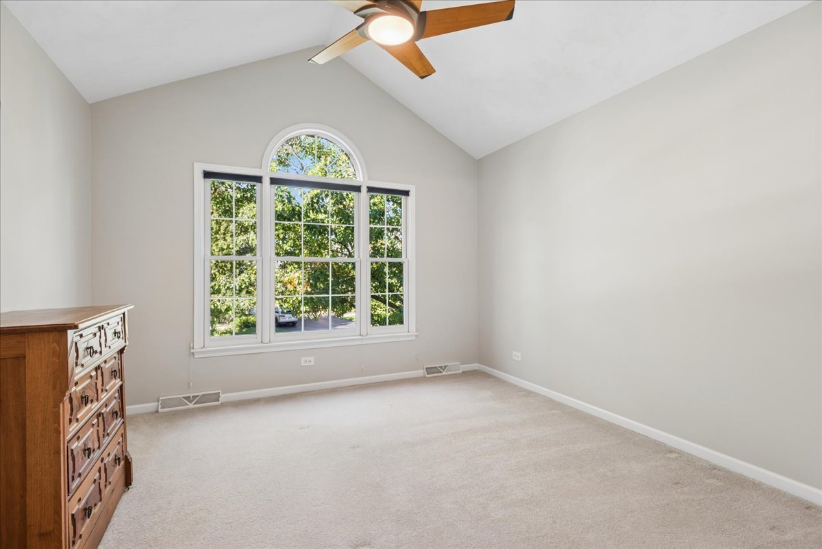 Bedroom with a vaulted ceiling, ceiling fan, and large arched window overlooking leafy trees.