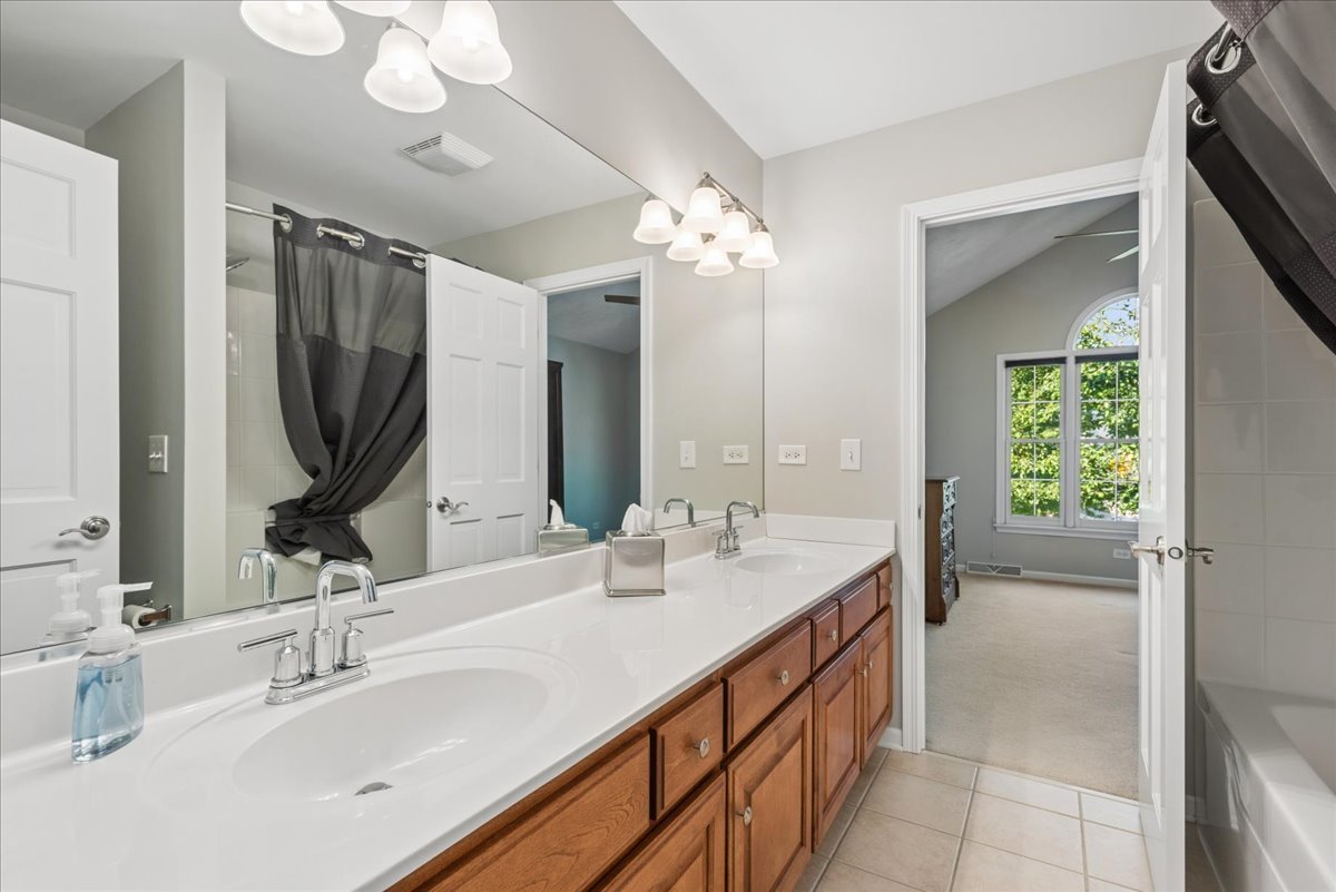 Bathroom with a long double-sink vanity, warm wood cabinets, and a large mirror.
