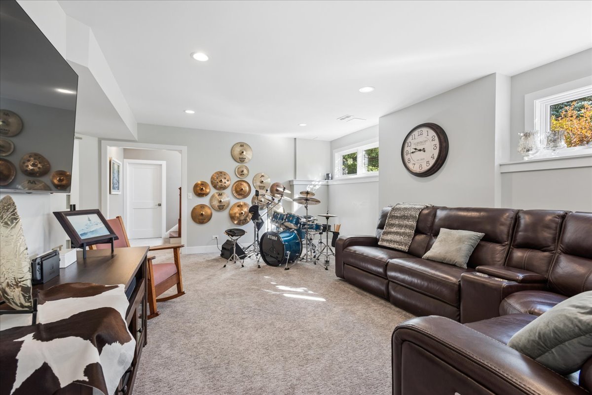 Furnished living room with a blue drum kit, wall-mounted cymbals, and brown leather sectional.