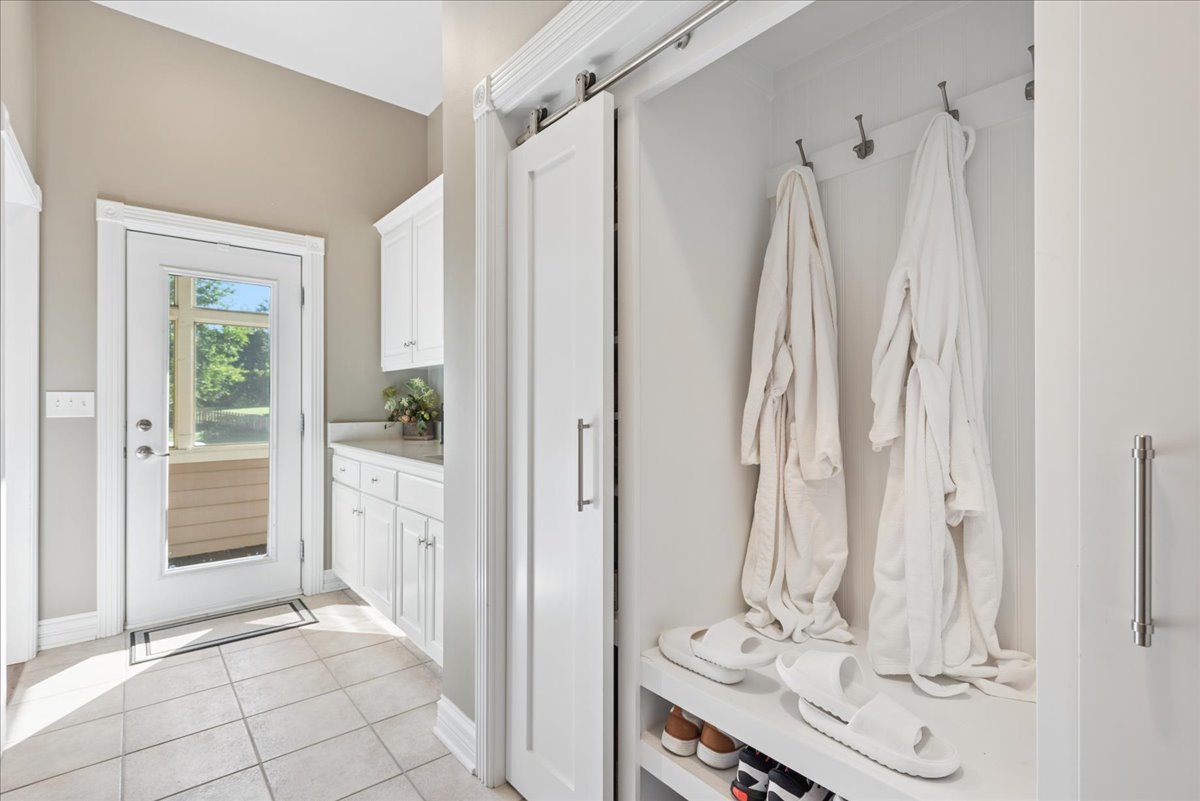 Mudroom with white built-in storage, robes hanging above a bench, and a glass exterior door.