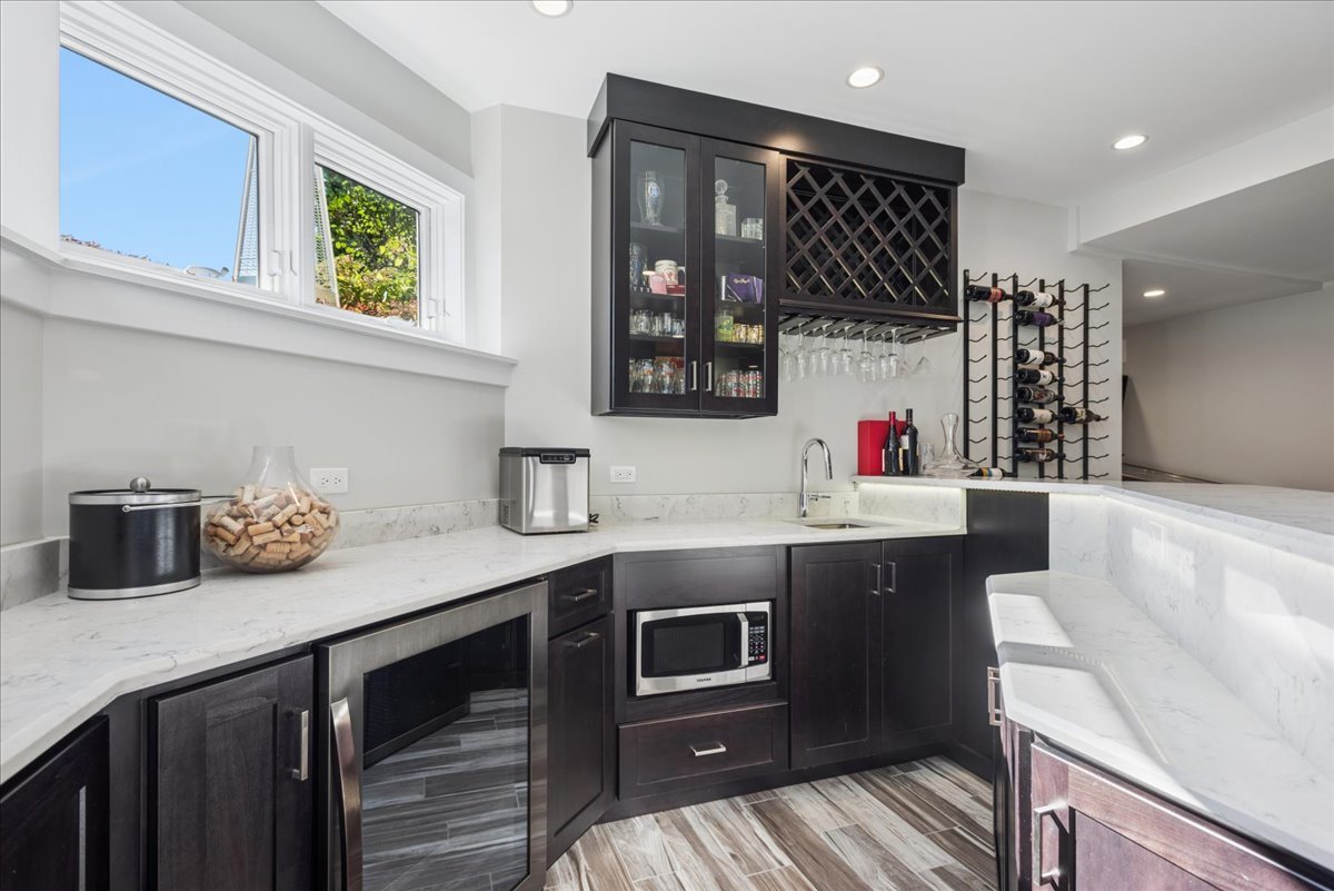 Bar area with dark cabinetry, white stone counters, built-in appliances, and wine racks.