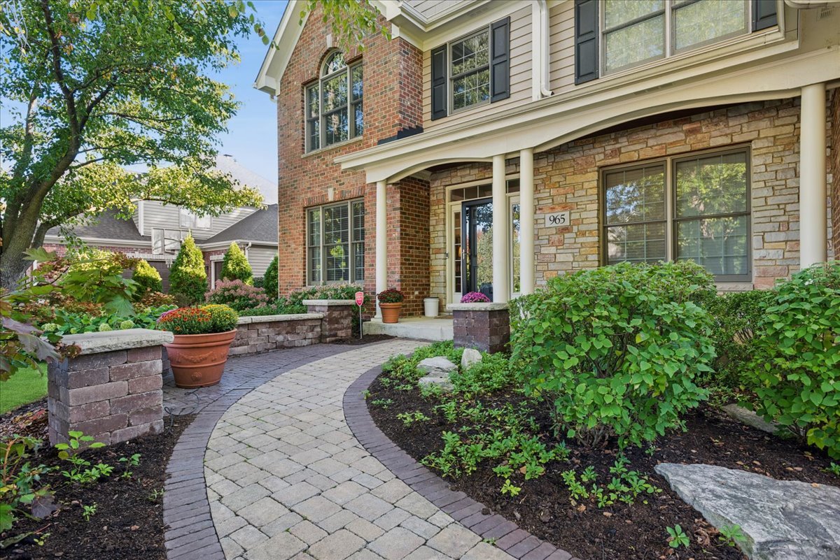 Two-story brick and stone home with a curved paver walkway and landscaped front garden.