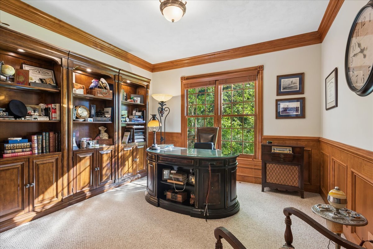 Home office with built-in wood bookcases, paneled walls, and a curved executive desk by a garden-facing window.