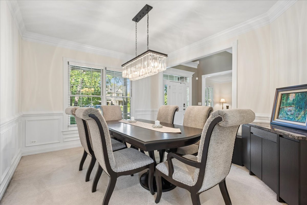 Dining room with a dark table, upholstered chairs, and a rectangular chandelier.