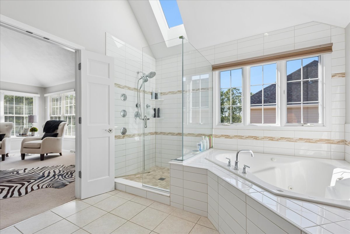 Bright bathroom with a corner soaking tub, glass shower, and skylight.