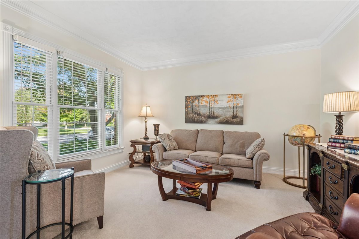 Living room with a beige sofa, oval glass-top coffee table, and large windows with white blinds.