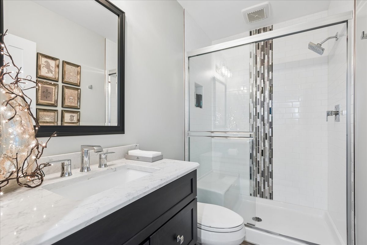 Bathroom with a marble-topped dark vanity and glass-enclosed tub and shower with a mosaic tile accent.