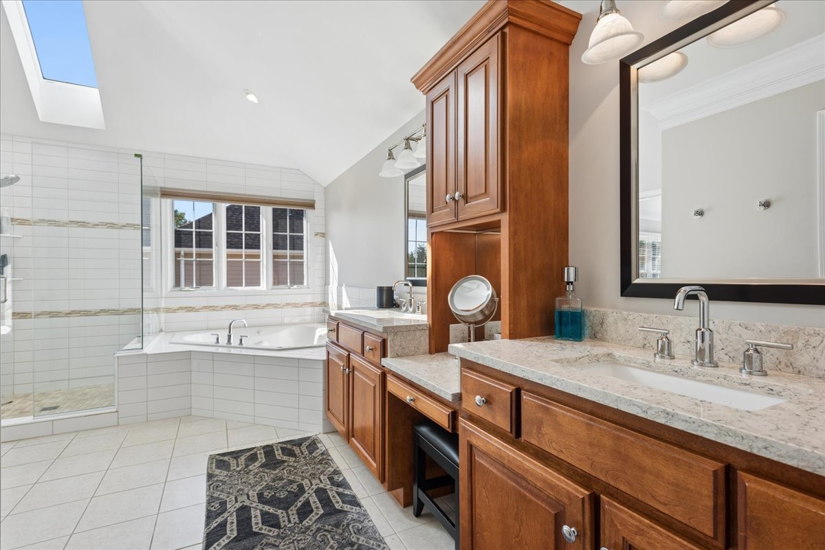 Primary bathroom with a skylight, glass shower, soaking tub, and long wood vanity.