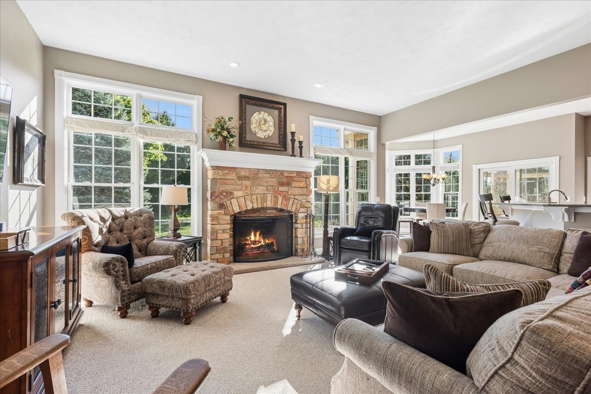 Living room with a stone fireplace, large windows, and sofas around a coffee table.