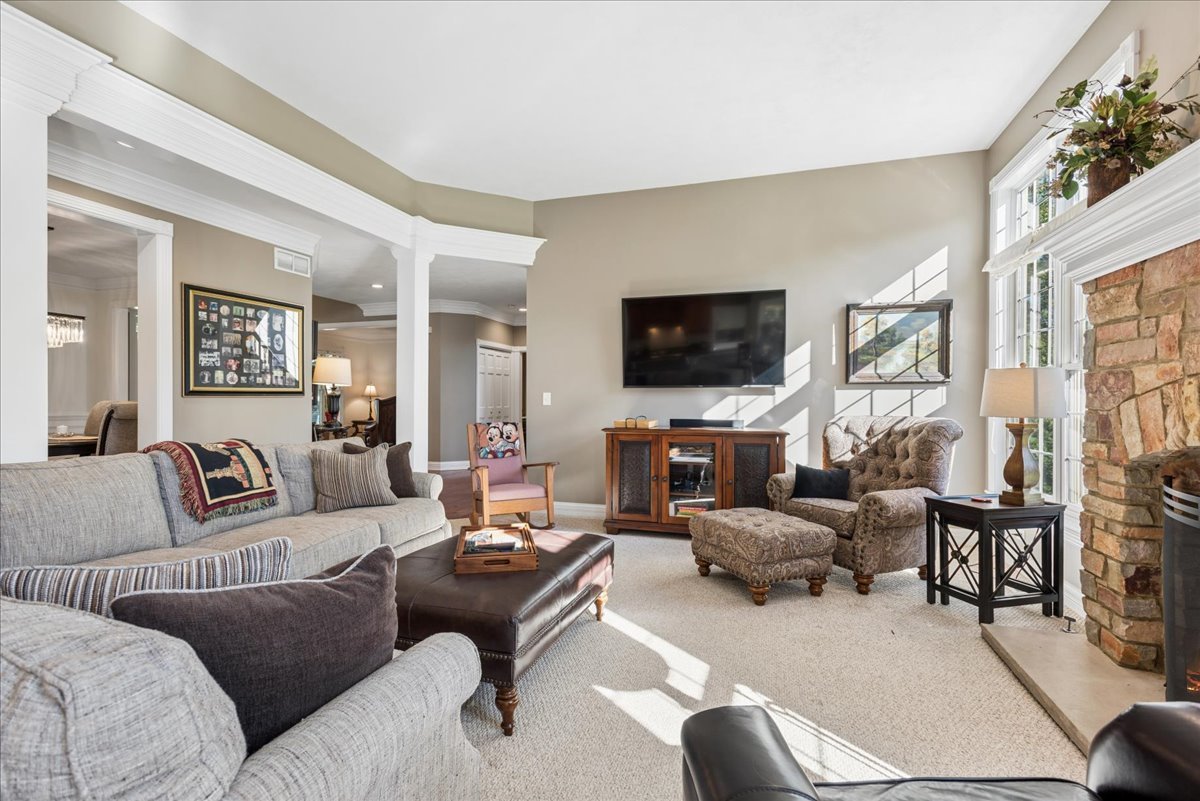 Furnished living room with gray sofas, a stone fireplace, and large sunlit windows.