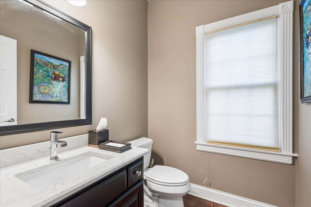 Bathroom vanity and toilet beside a large window with a closed blind.