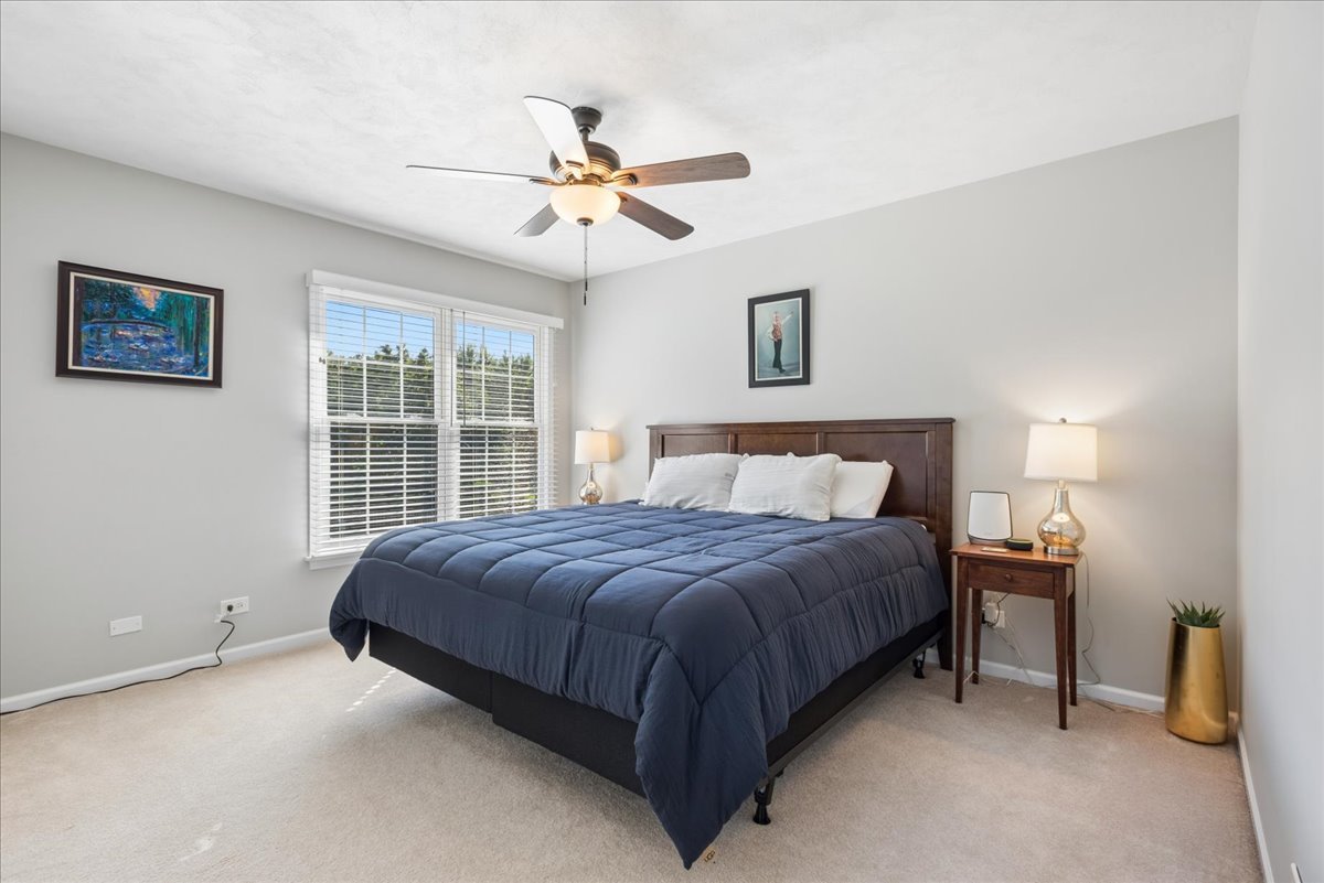 Bedroom with a navy-quilted bed, dark wood headboard, ceiling fan, and sunlit window.