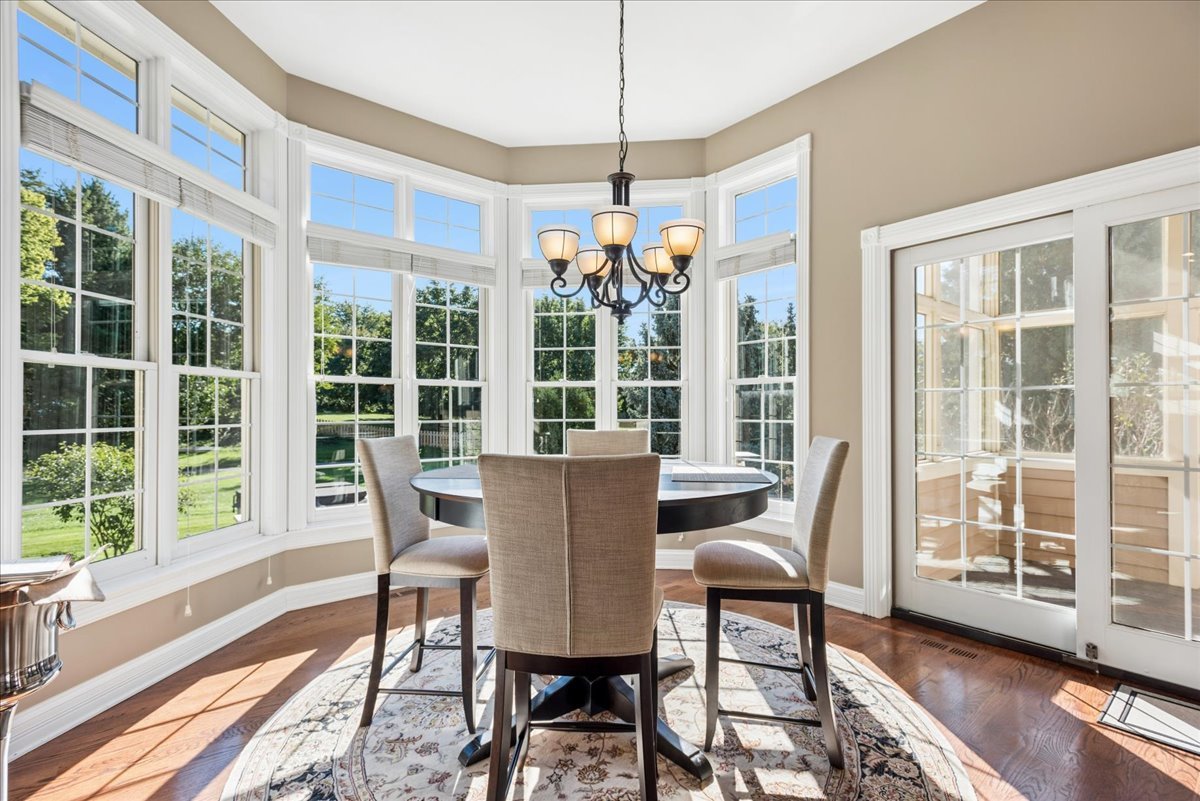 Dining room with a round table, chandelier, and large bay windows overlooking the lawn.