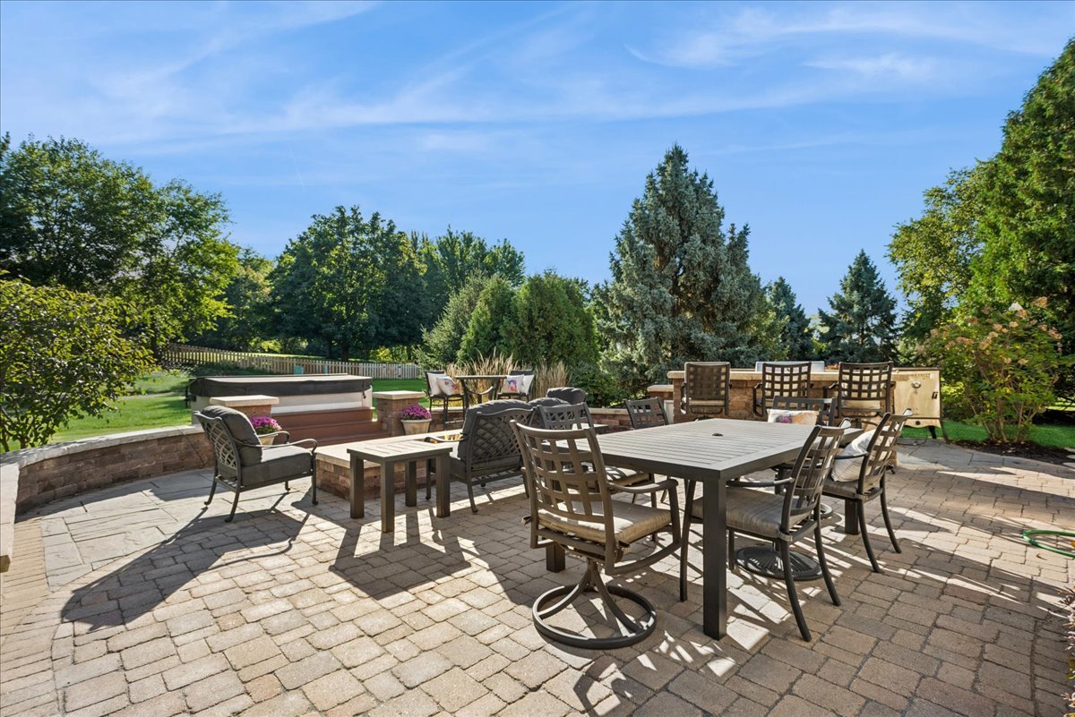 Backyard patio with a large dining set, cushioned seating, and a hot tub among mature trees.