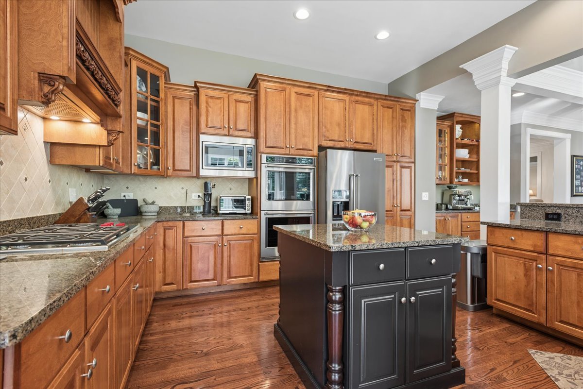 Kitchen with warm wood cabinetry, granite counters, a dark island, and stainless steel appliances.
