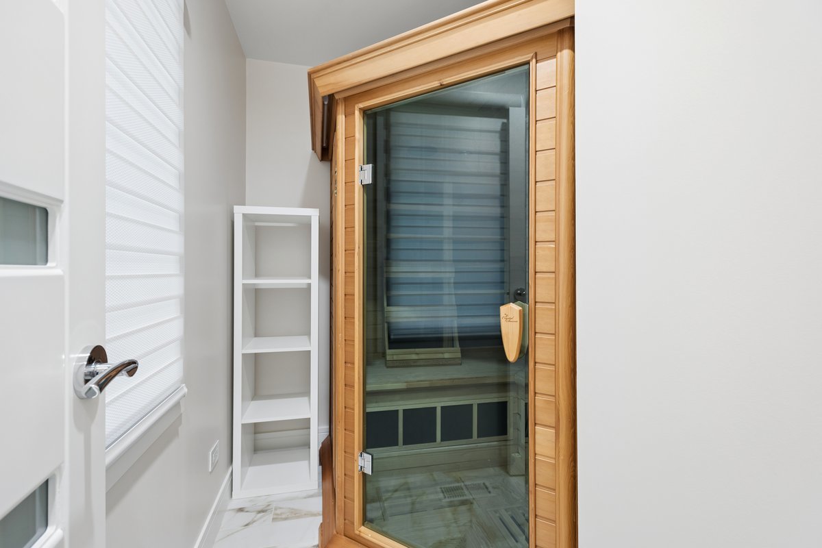 Home sauna with glass door, light wood surround, built-in bench, and marble-look tile floor.