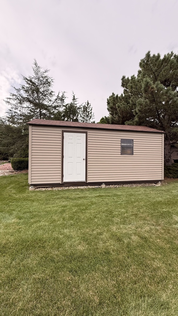Beige storage shed with a white door and single window on a grassy lawn.