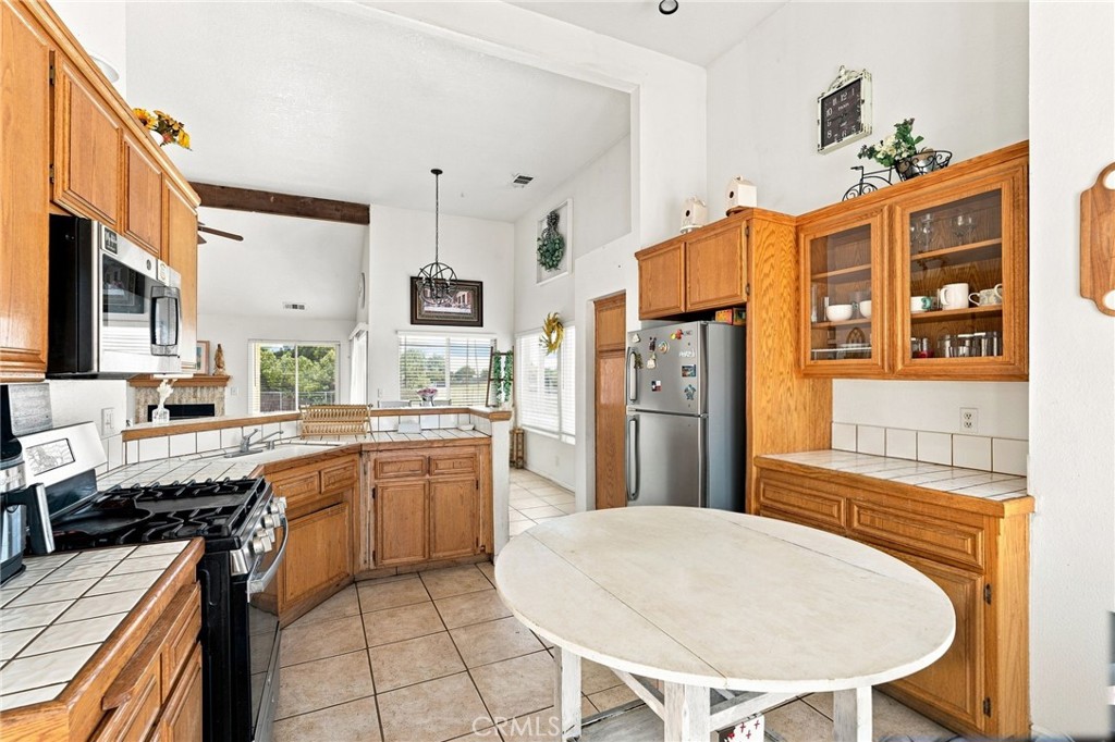 Kitchen with honey-colored wood cabinets, tiled counters, stainless steel appliances, and a large oval table.