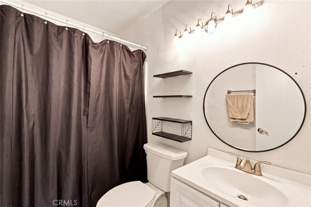 Bathroom with a white vanity, round mirror, toilet, and dark shower curtain.