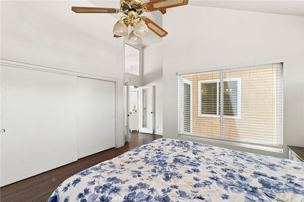 Bedroom with blue floral bedding, sliding closet doors, window blinds, and a ceiling fan.
