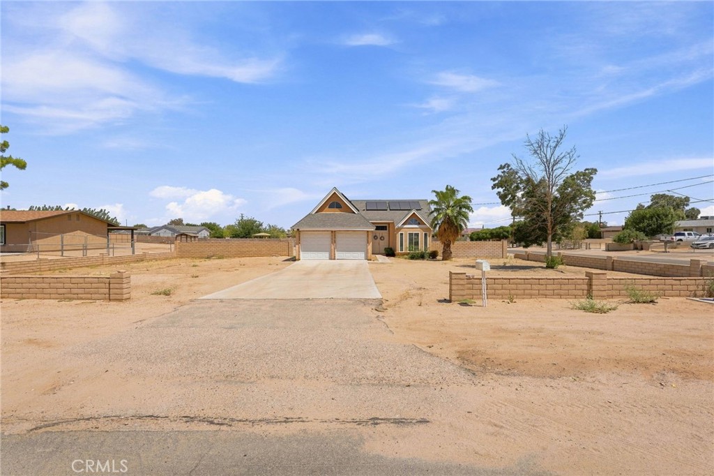 Tan single-story house with rooftop solar panels, a two-car garage, and a long driveway.
