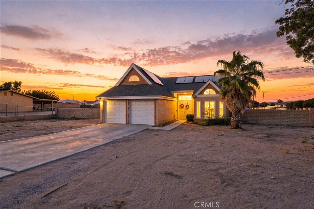 House exterior at sunset, with a two-car garage, solar panels, and a palm tree.