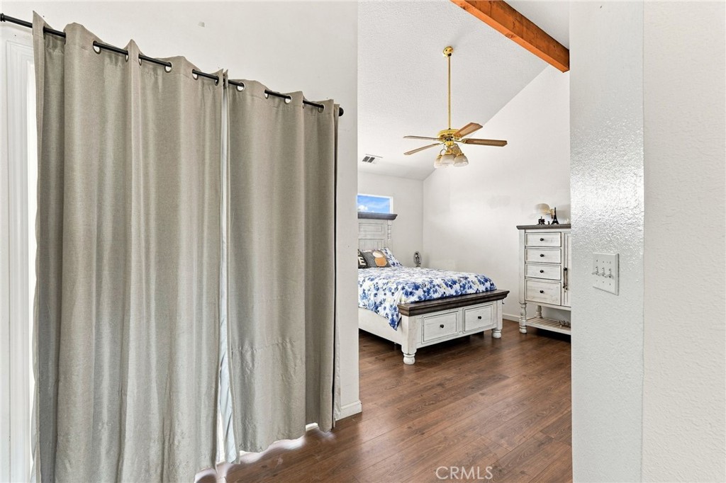 Bedroom with blue floral bedding, white furniture, gray curtains and wood flooring.