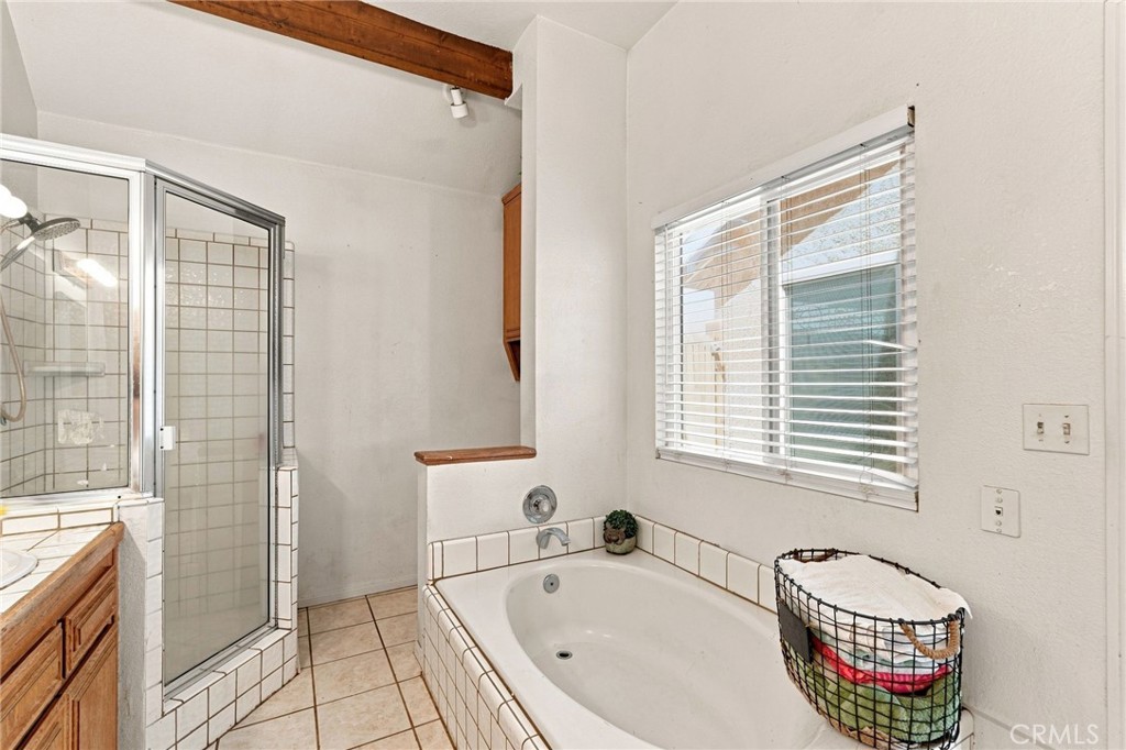 Bathroom with a tiled soaking tub beside a glass-enclosed shower and window blinds.