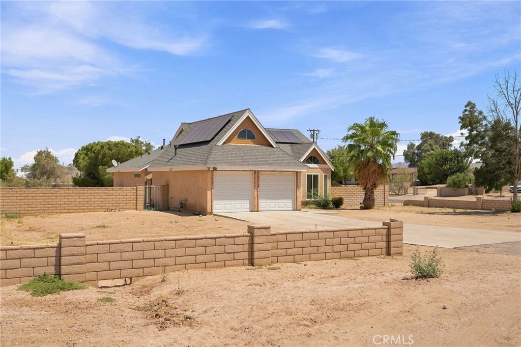 Tan single-story home with two white garage doors, a gabled roof, and a low block wall around the dry yard.