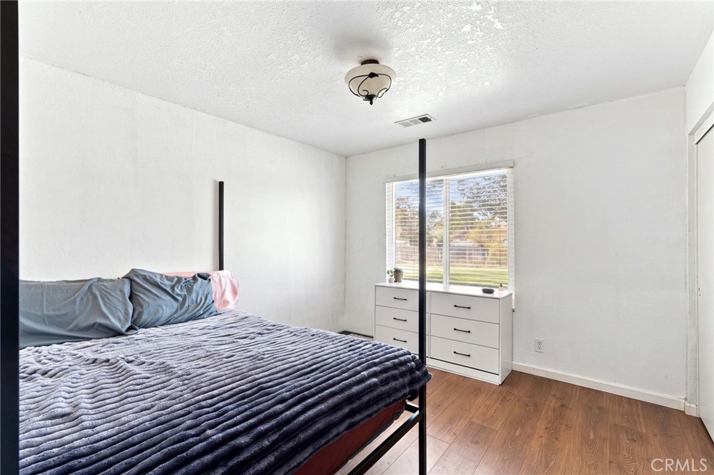 Bedroom with a large bed, wood-look flooring, and a window with blinds.