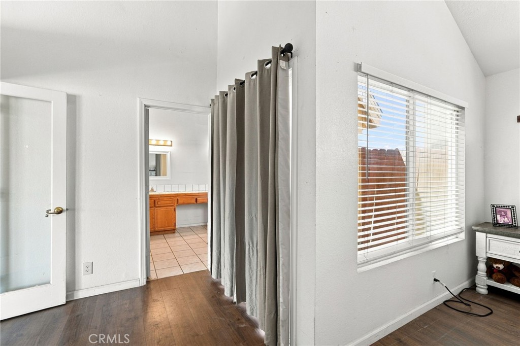 Bedroom with gray curtains and a large window, viewed toward an open bathroom doorway.