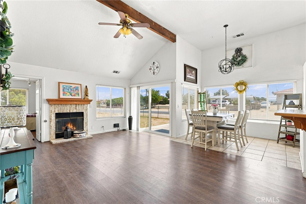 Open living and dining area with vaulted ceiling, exposed beam, fireplace, and large windows.