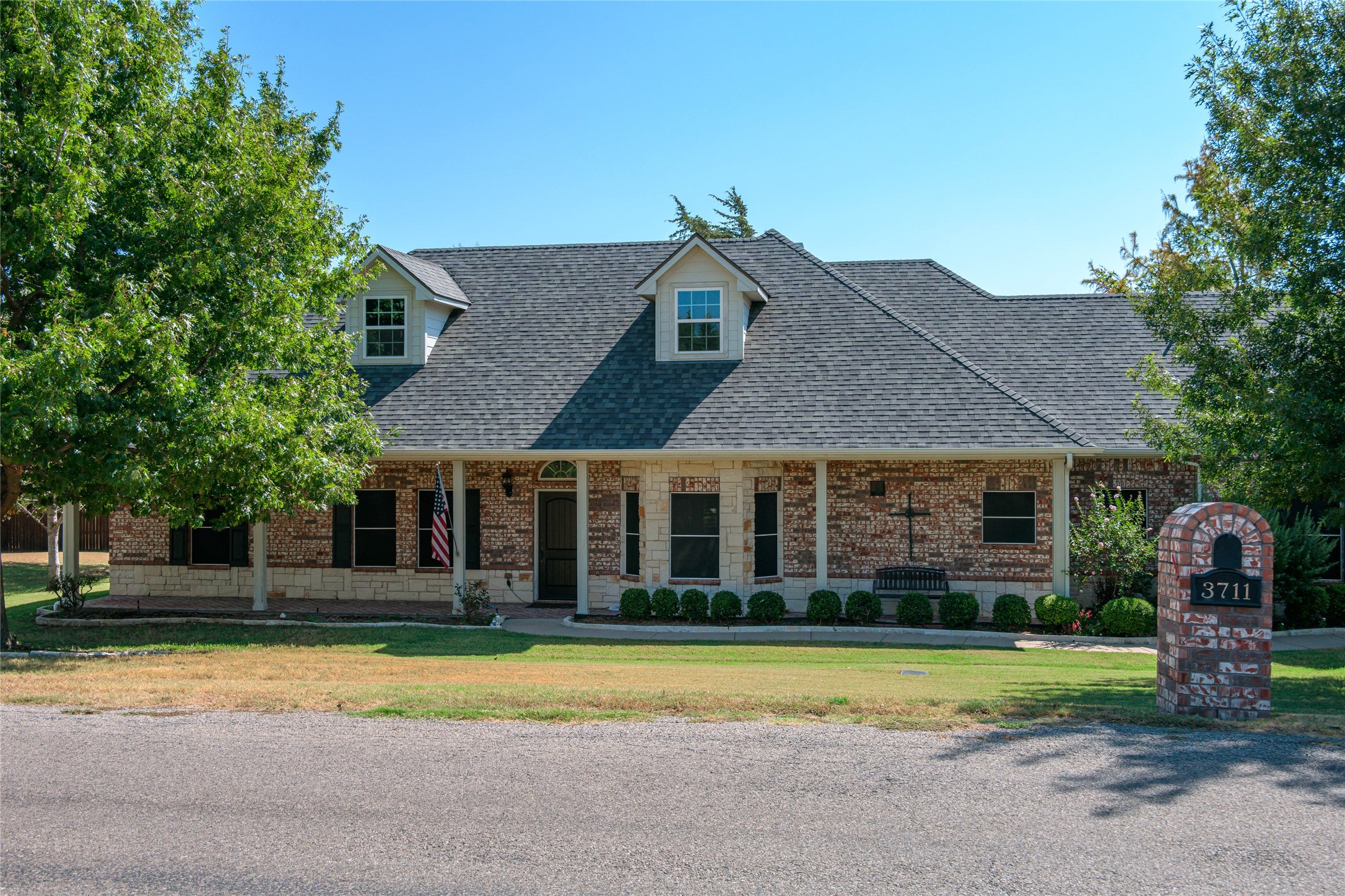 Brick-and-stone house with a broad shingle roof, covered porch, and brick pillar marked 3711.