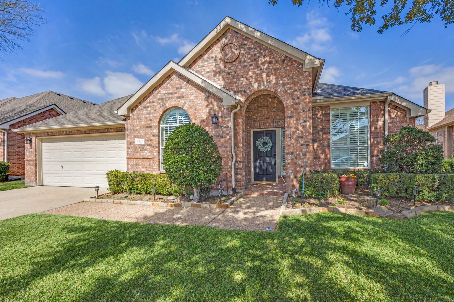 Red brick house with an attached white garage, arched window, and landscaped front yard.