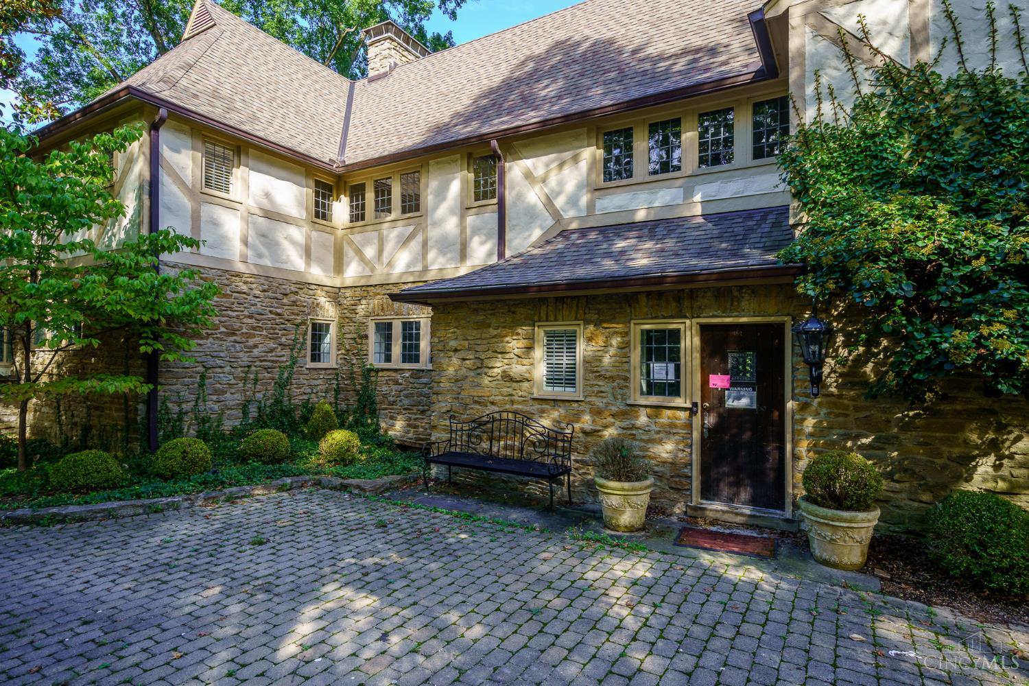 Two-story stone-and-timber house with a cobblestone courtyard and garden bench.