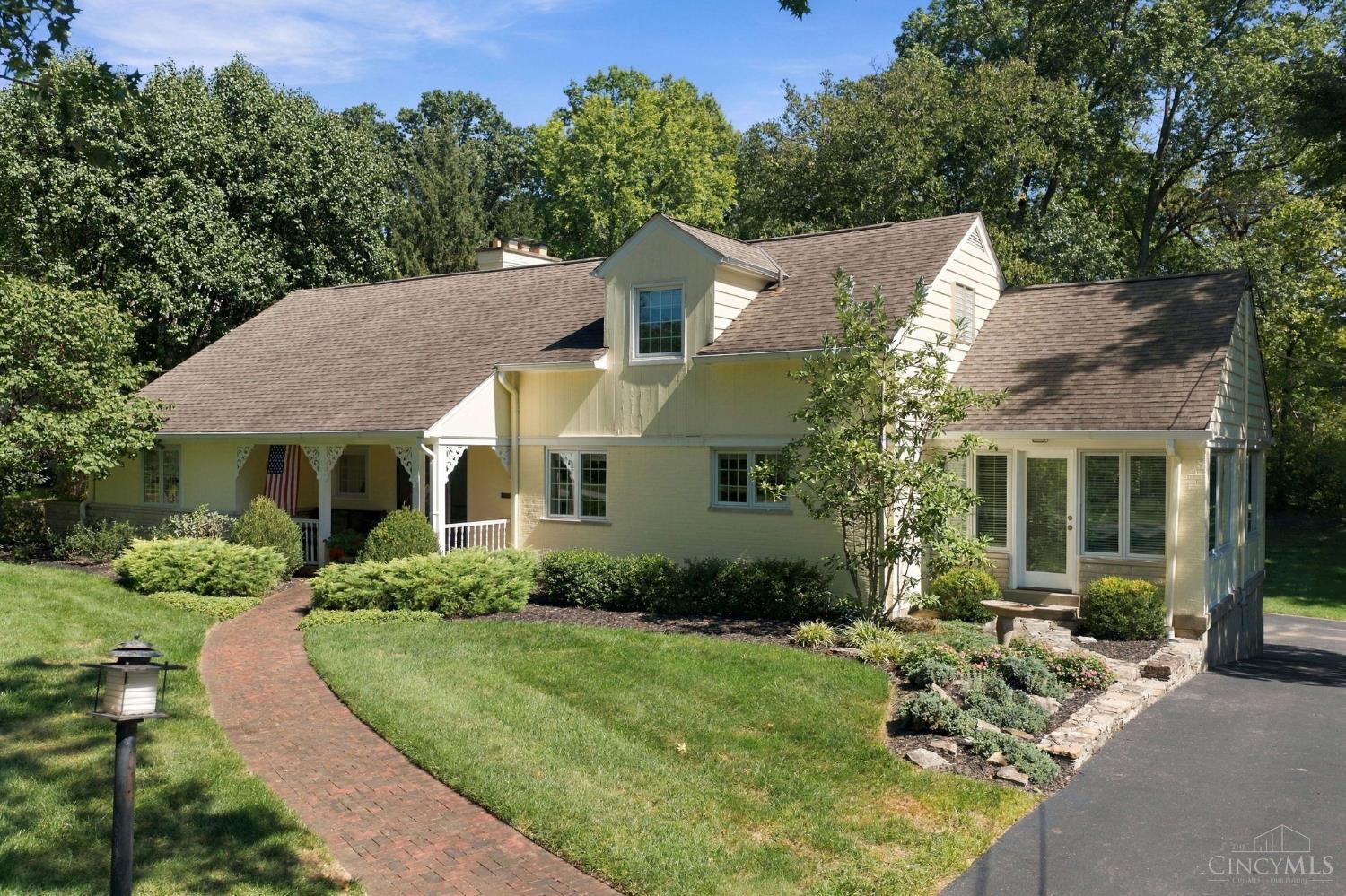 Cream house with multiple gables, a covered porch, landscaped yard, and curved brick walkway.