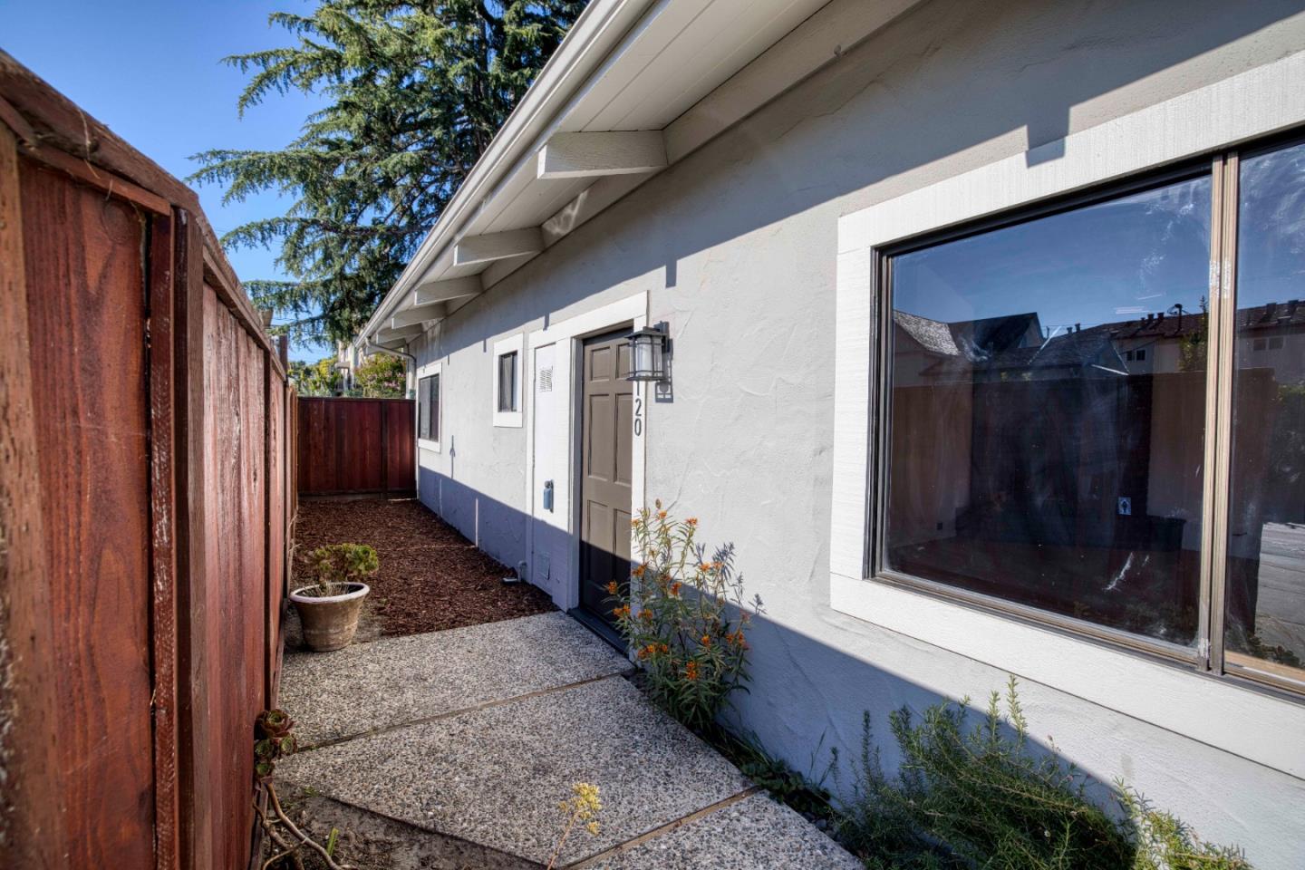 Home’s side entrance and window beside a concrete walkway and tall redwood fence.