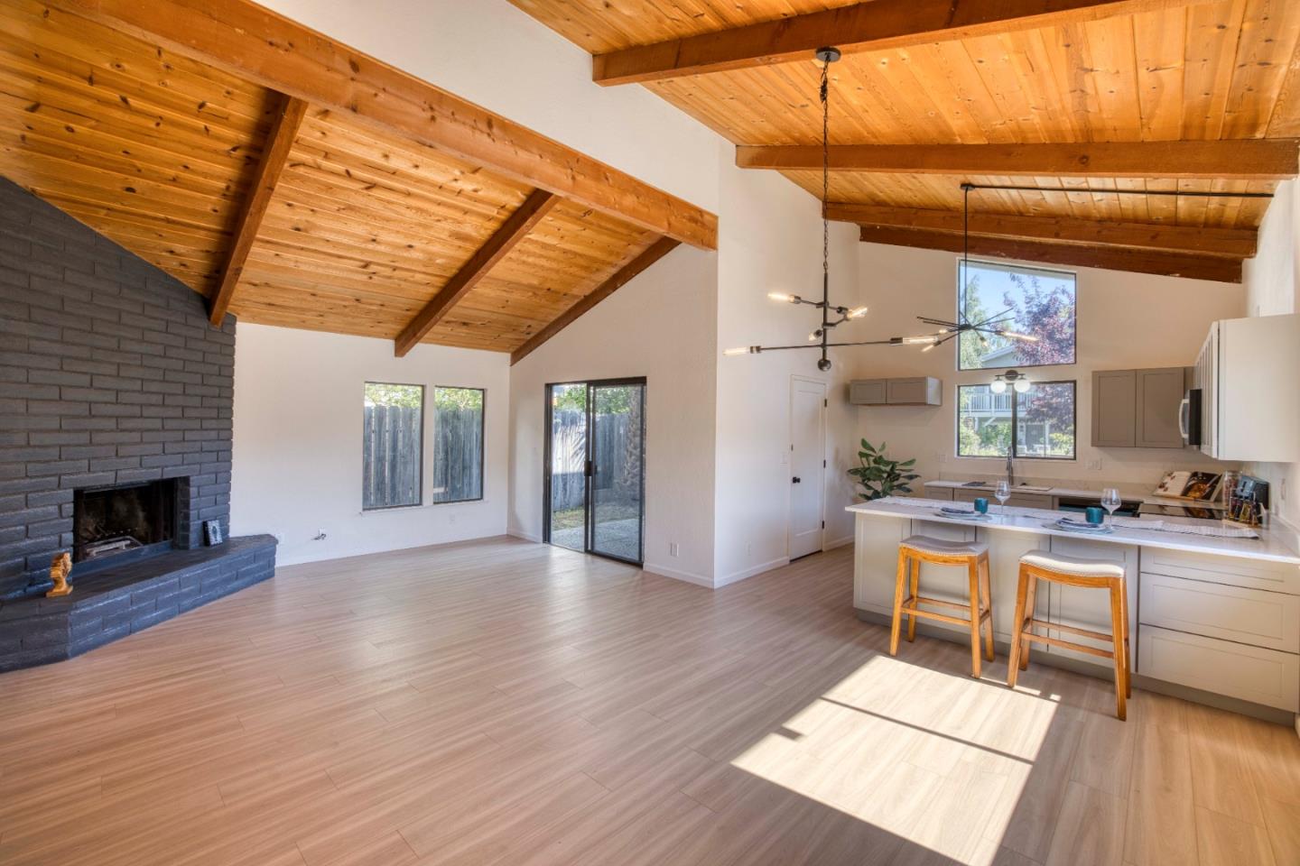 Open-plan living room and kitchen with a vaulted wood ceiling, brick fireplace, and island.