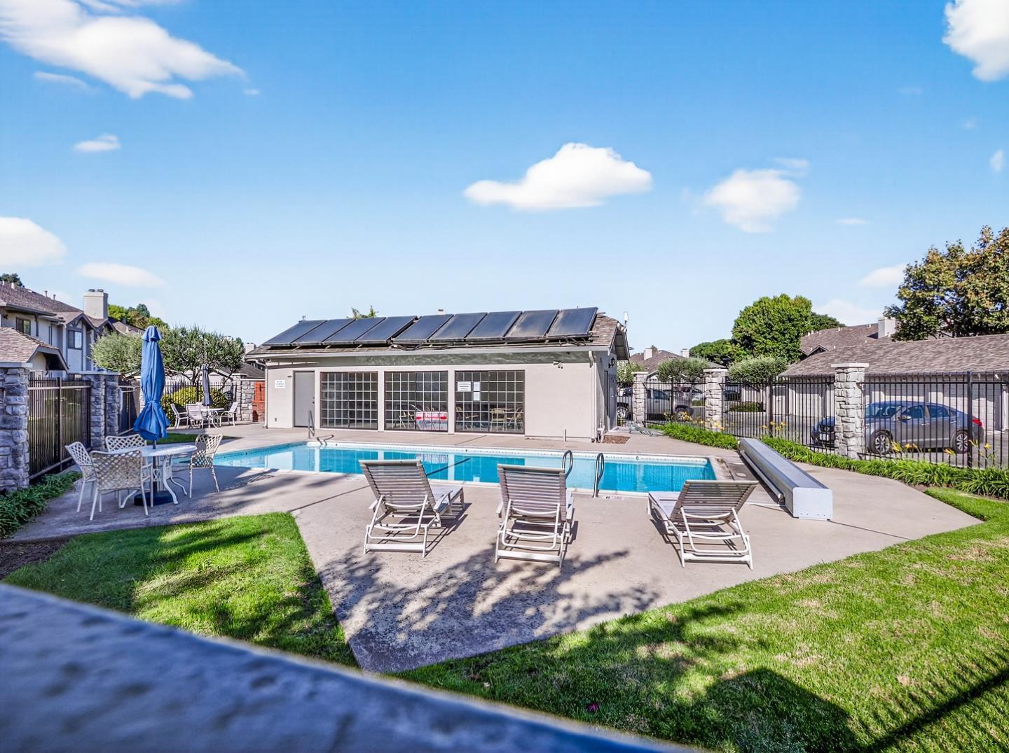 Residential complex pool with lounge chairs, patio seating, and solar panels on the pool building.