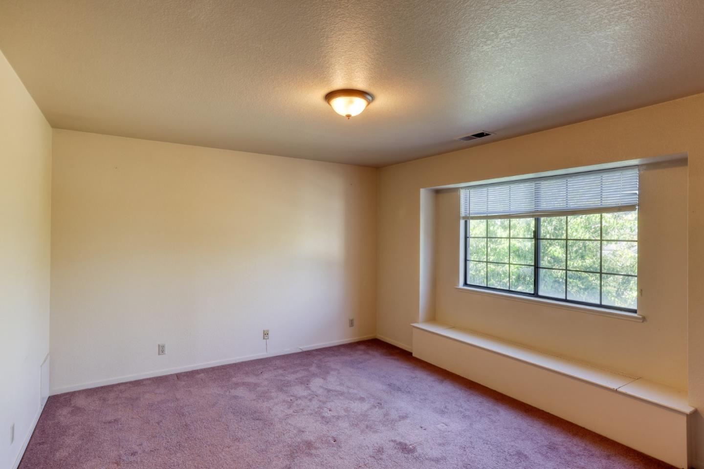 Empty carpeted room with a wide window and built-in window seat.